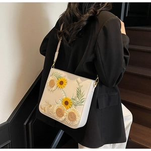 Detail of white leather shoulder bag featuring 3D sunflower embroidery and gold hardware