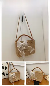 Close-up of khaki woven straw bag featuring white lace bow and imitation pearl details