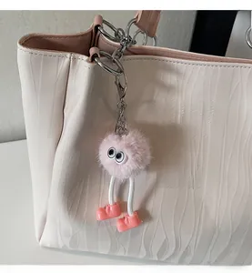 Detail of pink faux fur monster charm with big eyes on a white textured tote bag