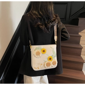 Detail of cream bucket bag featuring 3D sunflower embroidery and ethnic woven strap