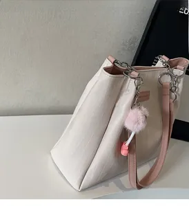 Detail of cream tote bag featuring wave texture, pink straps, and fluffy charm accessory