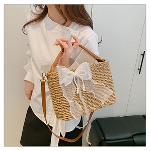 Detail of woven straw bag with white lace bow, pearl accents and brown leather strap