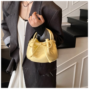 Close-up of bright yellow oil wax leather bucket bag with bow detail on a fashion model