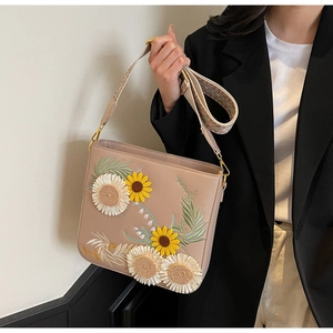 Detailed embroidery of sunflowers and daisies on a beige crossbody bag with woven strap