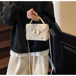 Chic cream leather box bag with gold oval buckle shown in a stylish lifestyle setting