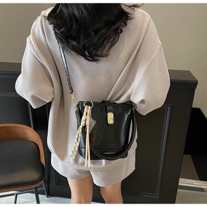 Détail d'un sac seau noir avec fermoir doré et gland tissé sur une bandoulière