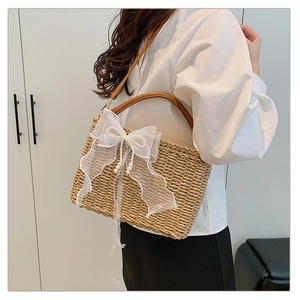 Detail of hand-woven straw bag featuring a large white lace bow and pearl pendant