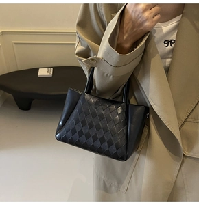 Detailed macro view of black leather tote bag featuring woven lattice texture and smooth side panels
