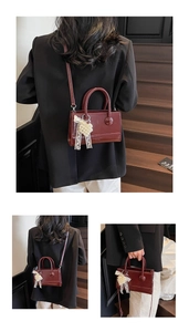 Detail view of burgundy handbag with pearl bow charm and embossed lettering detail