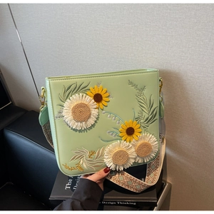 Close-up of light green crossbody bag with sunflower embroidery and wide woven strap