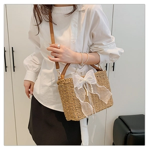 Detail of woven straw bag with white lace bow and pearl accents on a female model