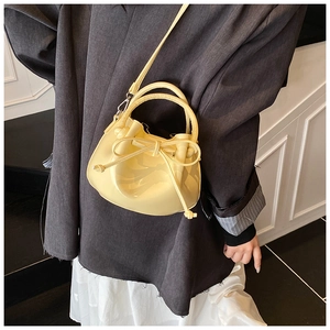 Pale yellow leather bucket bag with bow detail worn by model with grey blazer