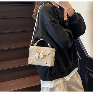 Detail view of cream white box bag with metallic oval twist lock and gold corner rivets