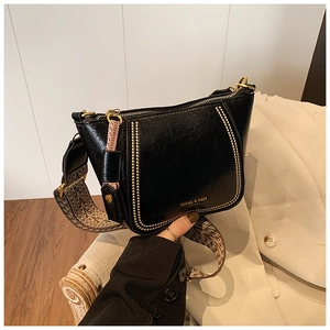 Detail of a black leather handbag featuring gold studs and a geometric woven strap