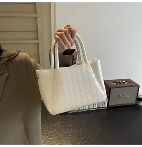 Close-up of off-white quilted bucket bag with metal buckle detail held by a person