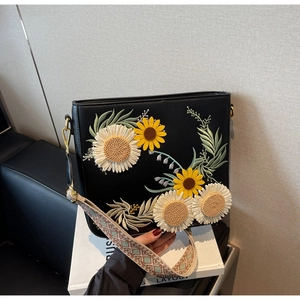 Detail of sunflower and daisy embroidery on black leather shoulder bag with woven strap