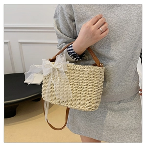 Detail of hand-woven straw bag featuring a large tulle bow with elegant pearl accents