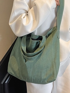 Minimalist green canvas tote bag with wide shoulder strap shown on model for daily use
