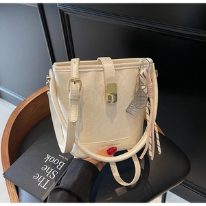 Détail du sac seau crème montrant le fermoir doré et le charm raquette de tennis tissé