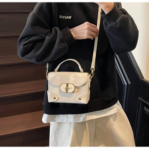 Detail view of cream white patent leather box bag with gold buckle and metal studs