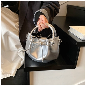 Detail view of a silver bucket bag with bow drawstring and glossy metallic texture