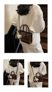 Detail of dark brown square bag featuring pearl bow charm and dual cylindrical handles