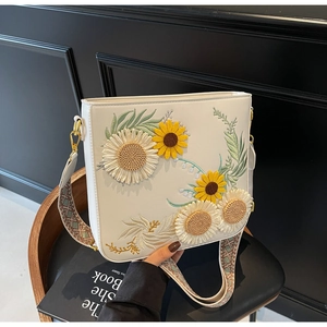 Close-up of white bucket bag featuring 3D sunflower embroidery and a woven wide strap