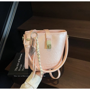 Sac seau rose avec texture litchi et fermoir doré sur un escalier en bois