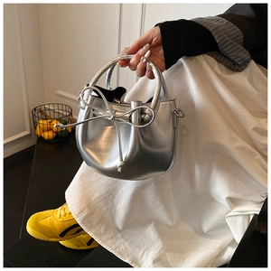 Detail of silver metallic bucket bag with ribbon bow and round handle held by a model