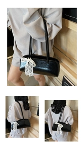 Detail der schwarzen glänzenden Baguette-Tasche mit weißem Spitzen-Schleifen-Anhänger