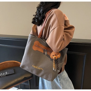 Detalle del bolso tote de lona gris oscuro con correas de cuero marrón y colgante de perrito