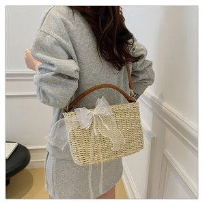 Detail view of woven beige straw bag featuring a white organza bow and pearl accents