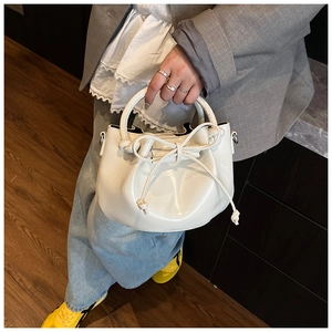 Detail of white oil wax leather bucket bag with bow drawstring and sleek handle grip