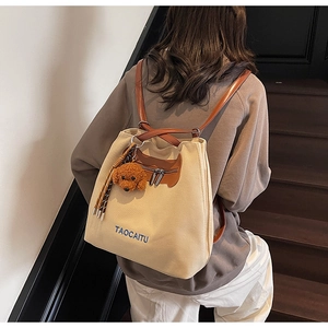 Detalle de la mochila de lona beige con correas de cuero marrón y colgante de peluche