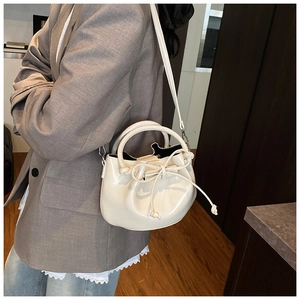 Chic cream bucket bag in glossy faux leather worn crossbody with adjustable strap