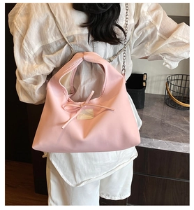 Detail of pink nylon shoulder bag featuring a decorative bow and silver chain strap