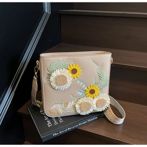 Detail of sunflower embroidery on beige leather bucket bag with woven shoulder strap