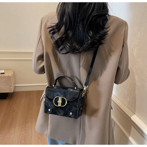 Model wearing black glossy crossbody box bag with gold buckle and brown blazer outfit