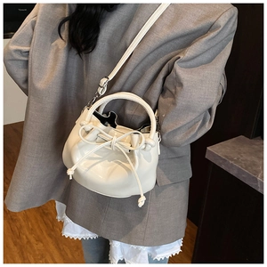 Chic white oil wax leather bucket bag with a bow detail, held by a model in a grey blazer