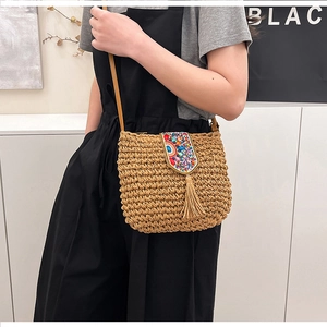 Straw crossbody bag featuring colorful ethnic beadwork and tassels shown on a model
