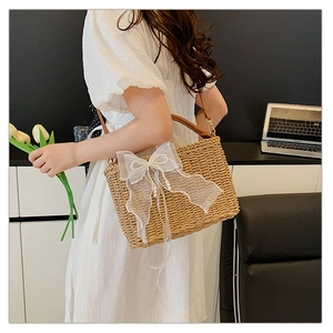 Detail of straw woven handbag featuring a white organza bow and pearl embellishments
