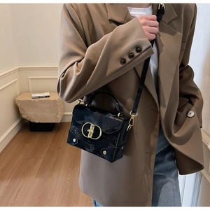 Detail of glossy black handbag with golden oval metal lock and elegant texture on faux leather
