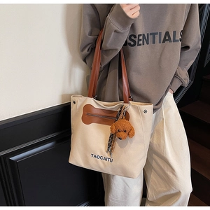Detalle del bolso de lona con asas de cuero marrón y un colgante de perro de peluche