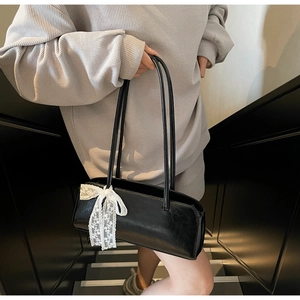 Detail der schwarzen Baguette-Tasche aus Kunstleder mit weißer Spitzenschleife
