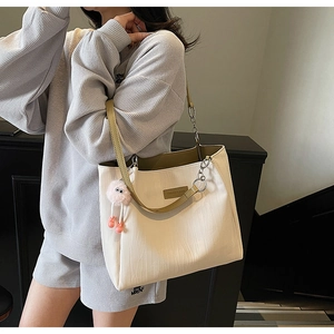 Detail of off-white tote bag with wave texture, metal chain, and cute pink charm