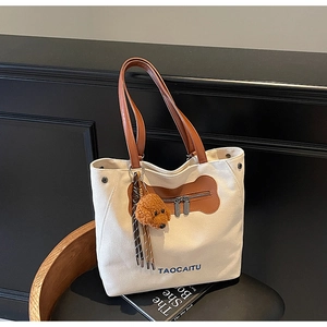 Detalle del bolso tote de lona con asas de cuero y un colgante de peluche de perrito