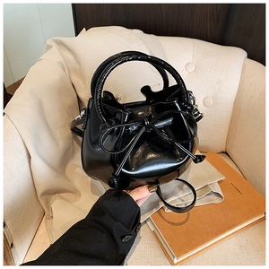Detail of black glossy leather bucket bag with decorative bow and top handle on sofa
