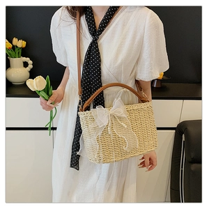 Detail of woven straw bag with lace bow and pearl tassels on a leather shoulder strap