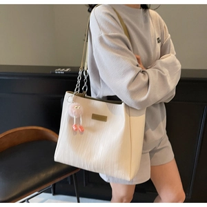 Detail of cream tote bag with wave texture, silver chain strap and pink fuzzy charm