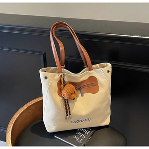 Detalle del bolso tote de lona beige con asas de cuero marrón y colgante de osito